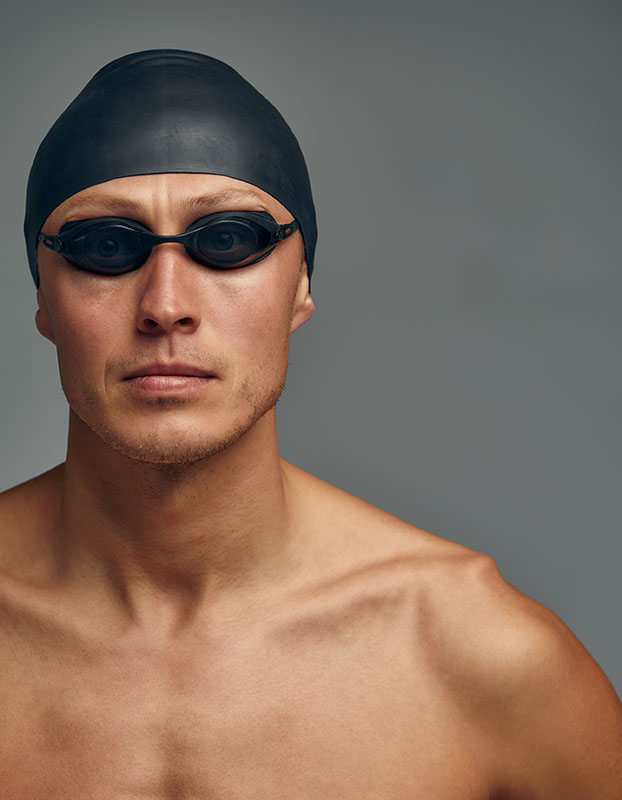 Portrait of a swimmer in a cap and mask, half-length portrait, young athlete swimmer wearing a cap and mask for swimming, copies of space, gray background.